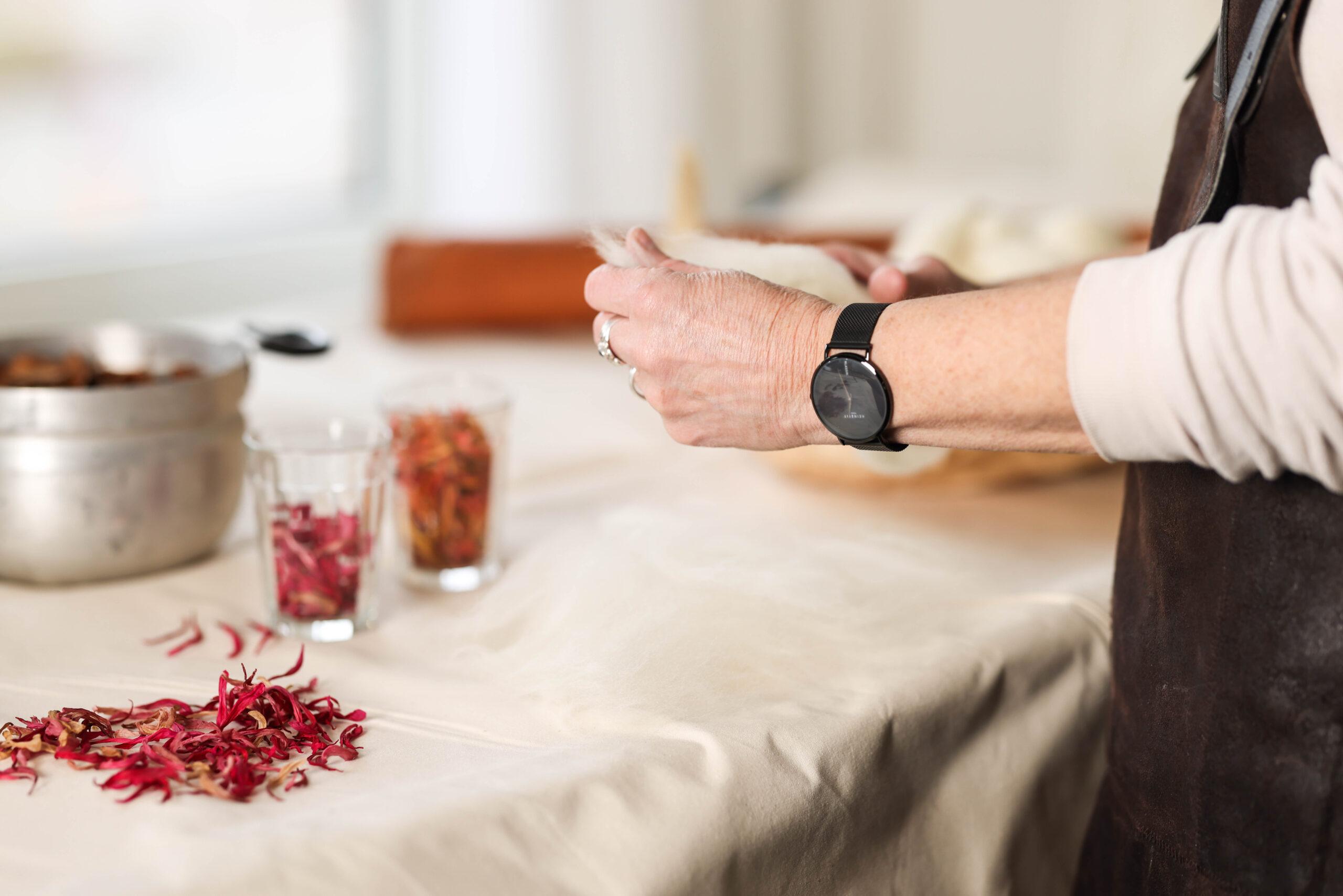 Mevrouw die wol in haar handen heeft en aan de tafel met spullen staat